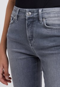 Jeans de mezclilla gris con un diseño ajustado, cinco bolsillos y una sutil textura desgastada. Presentan un cierre de botón metálico y costuras en contraste.