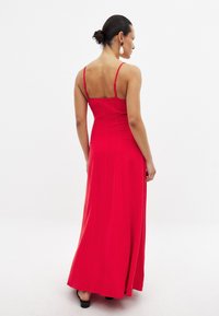 Röd, ärmlös maxiklänning med figursydd överdel och flödande kjol. Har tunna band och en mjuk, slät textur. Baktill syns klänningen.