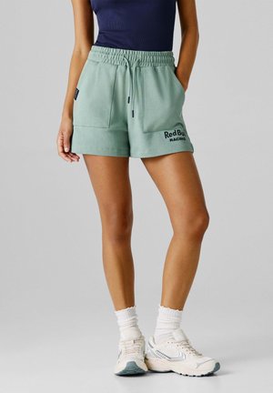 Hellgrüne Sportshorts mit elastischem Bund, zwei Taschen und "Red Bull Racing" aufgestickt in Marineblau. Kombination mit weißen Sneakern.