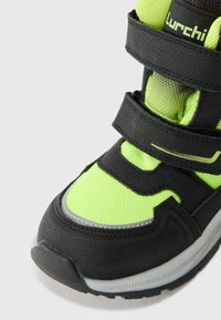 Sorte og neongrønn sneakers med mesh- og syntetiske materialer, to justerbare borrelåsremmer og en teksturert gummisåle.