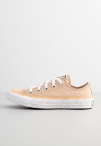 Baskets en toile beige avec des lacets blancs, une semelle en caoutchouc parsemée de taches orange et grises, et un design à profil bas. Embout contrastant en couleur.