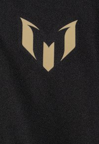Zwarte stof met een gestructureerd oppervlak en een prominent gouden logo ontwerp dat lijkt op gestileerde vleugels of een schild in het midden.