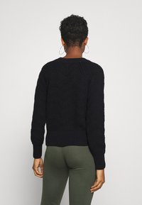 Maglione nero a maglia con motivo a zig zag, polsini e cintura a costine. Il design è texturizzato e si adatta saldamente al torso.