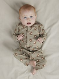 Grön heldragt med mönster av brunbjörnar, långärmad, med tryckknappar fram och fickmanschetter, buren av en baby mot en ljus bakgrund.