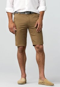 Shorts beiges à coupe ajustée, fabriqués en tissu léger. Associés à une ceinture bleue à motifs et à des espadrilles beiges.