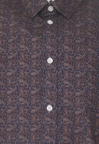 Dunkelblaue Hemd mit braunem Paisleymuster und weißen Knöpfen, zeigt Kragen und knopfbare Vorderseite.