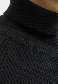 Suéter negro de punto acanalado con un alto cuello de tortuga. La textura es ajustada y tejida, y presenta patrones de costura visibles.