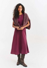 Sukienka w kolorze malwy o zwiewnym fasonie, zestawiona z puchatym, głęboko śliwkowym płaszczem. Modelka ma na sobie brązowe zamszowe kozaki za kolano z bocznymi klamrami.