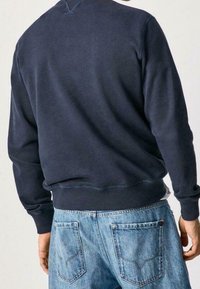 Navy sweatshirt with a rounded neckline and ribbed cuffs, paired with light blue denim jeans featuring back pockets and a distinct stitching pattern.