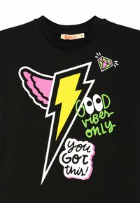Schwarzes Baumwoll-T-Shirt mit bunten Drucken: ein gelber Blitz, pinke Flügel und der Text "GOOD VIBES ONLY" in Grün mit einem Diamant-Graphic.