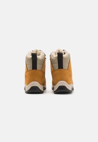 Rudos zomšos žygių batai su smėlinės spalvos tekstiliniu viršumi, tekstūruota pamušalu, juodu galiniu traukimo dirželiu ir guminėmis padais. Įspaustas Timberland logotipas.