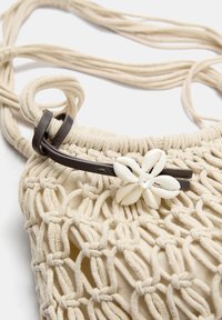 Borsa all'uncinetto color tan con un accento floreale a forma di conchiglia, dotata di una tracolla in pelle marrone e una finitura morbida e testurizzata.