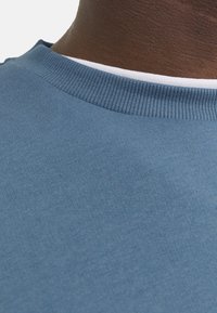 T-shirt en coton bleu à col rond avec un col ribbed, présentant un détail de finition blanche. Texture lisse, montrant un gros plan du tissu.