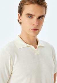 Lyscreme polo shirt med en blød tekstur, korte ærmer og en klassisk krave med et subtilt v-hals design.