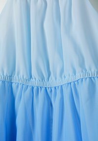 Rochie de culoare bleu deschis, cu un bust plisat și o fustă fluidă, stratificată. Fabricată dintr-un material translucid, ce are o textură netedă și moale.