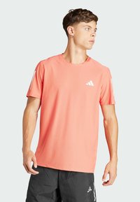 Camiseta deportiva coral fabricada con tejido transpirable, con cuello redondo y mangas cortas, y con acentos de logo blanco en el pecho y la manga.