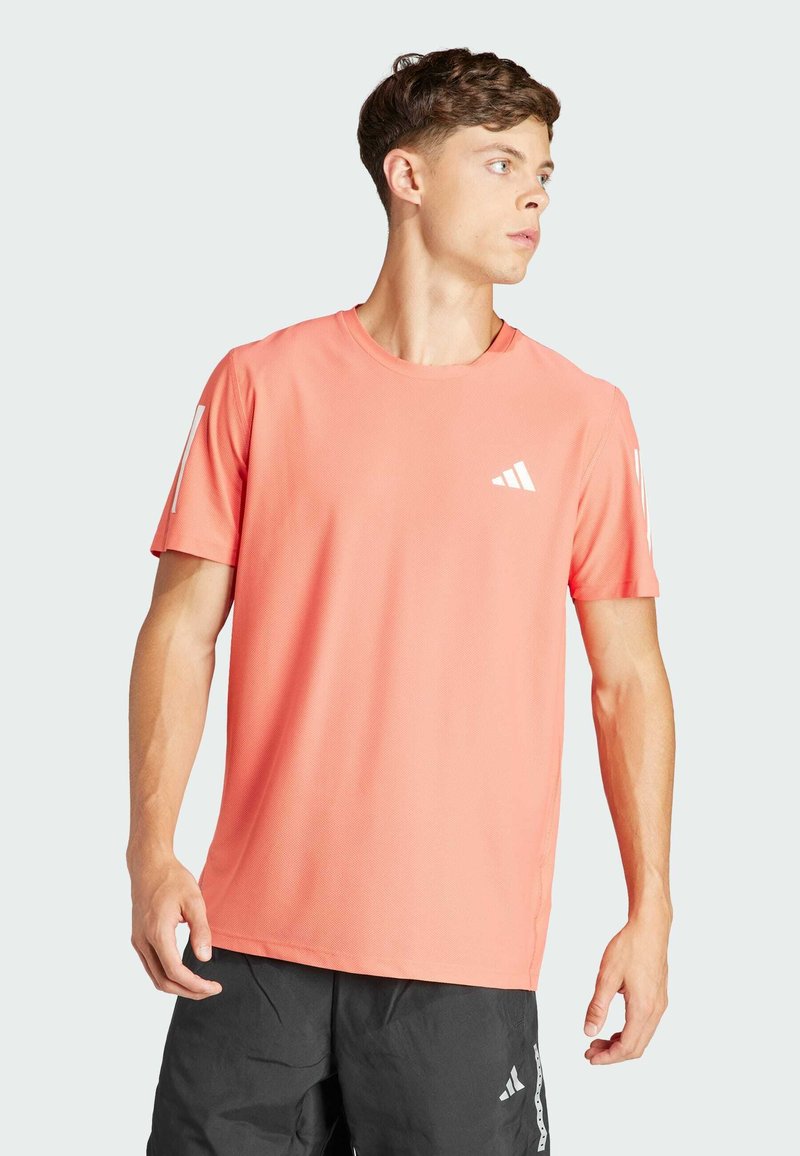 Camiseta deportiva coral fabricada con tejido transpirable, con cuello redondo y mangas cortas, y con acentos de logo blanco en el pecho y la manga.