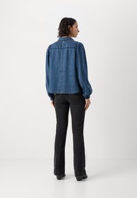 Mørkeblå denimjakke med puffede ærmer, knaplukning og let frynset kant, parret med sorte breddebukser og støvler med hæl.