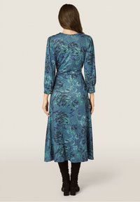 Langærmet kjole i nuancer af blå med blomster mønstre, der har en tætsiddende talje og en flagrende nederdel. Glat stof med knapdetaljer på ærmerne.