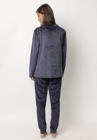 Conjunto de pijama de terciopelo azul marino que incluye una camiseta de manga larga con lunares blancos y pantalones a juego. Textura suave y corte relajado.