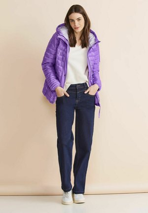 Giacca a vento viola con cappuccio, caratterizzata da un design trapuntato; abbinata a jeans a gamba dritta blu scuro e sneakers bianche.