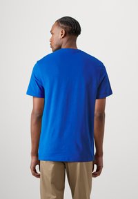 T-shirt a maniche corte in cotone blu brillante, con scollatura a girocollo e vestibilità comoda, con dettagli minimi. Indossato con pantaloni beige.