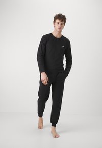 Black long-sleeve shirt and matching jogger pants in a soft fabric. Shirt features a small logo on the chest. Fitted and comfortable design.