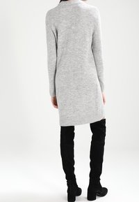 Abito in maglia grigia con maniche lunghe, orlo a costine e vestibilità rilassata, abbinato a stivali alti fino alla coscia in suede nero.