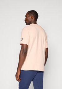 Lyserød kortærmet t-shirt lavet af blødt stof, med rund halsudskæring og et lille logo på venstre ærme. Glat tekstur.