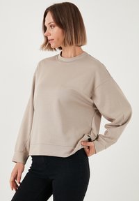 Felpa beige con collo rotondo, maniche lunghe e vestibilità rilassata. Realizzata in tessuto liscio con un design semplice e minimale.