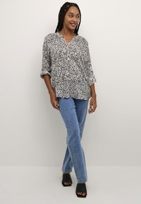 Svart och vit mönstrad blus med V-hals, trekvartsärmar, tillsammans med ljusblå raka jeans och svarta klackar med öppen tå.