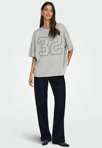 Szara, przeszła koszulka z nadrukiem czarnego konturu '32', zestawiona z ciemnoniebieskimi szerokimi dżinsami i czarnymi szpiczastymi butami z ćwiekami.