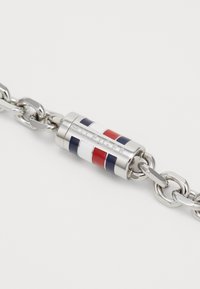 Silberne Metallkette mit einem zylindrischen Anhänger, der rot-, weiß- und blaugestreift ist und mit "HILFIGER" auf der Oberfläche graviert ist.
