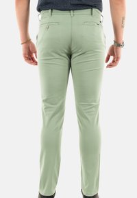 Pantalons vert clair avec une coupe slim, présentant une texture lisse, des passants de ceinture et deux poches arrière à boutons. Stylés avec une taille basse.