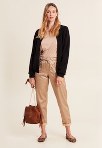Cardigan nero, top in satin beige, pantaloni in ecopelle beige con vita elastica, borsa in suede marrone con frange e ballerine con stampa leopardata.