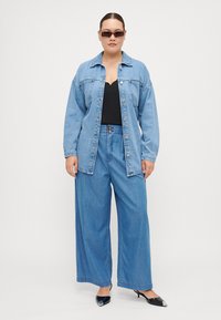 Light blue denim jacket, wide-legged light blue jeans, black top, and black pointed-toe shoes; paired with dark sunglasses, smooth texture.