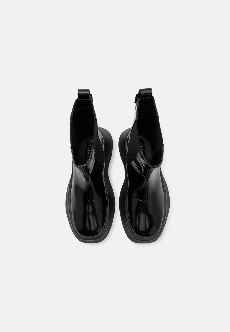 Czarne, błyszczące botki za kostkę z elastycznymi panelami bocznymi i pętelką, z okrągłym noskiem i masywną czarną podeszwą. Gładka tekstura na całej powierzchni.