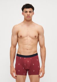 Burgundske bokserice z mornarsko modrim pasom, mehki bombažni material in ponavljajoč vzorec diamantov v beli barvi. Ozek kroj.