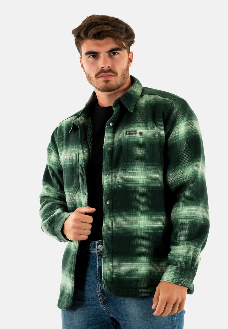 Chemise en flanelle à carreaux verts avec un col boutonné, poche poitrine et une texture douce. Portez-la avec un t-shirt noir en dessous.
