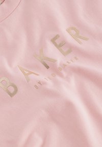 Roze katoenen t-shirt met opvallende gouden tekst "BAKER" en "by TED BAKER," met een zachte textuur en een ronde halslijn.