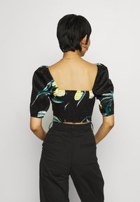 Donna con capelli corti e scuri che indossa un crop top nero con maniche a sbuffo e stampa floreale, abbinato a pantaloni neri a vita alta, vista da dietro.