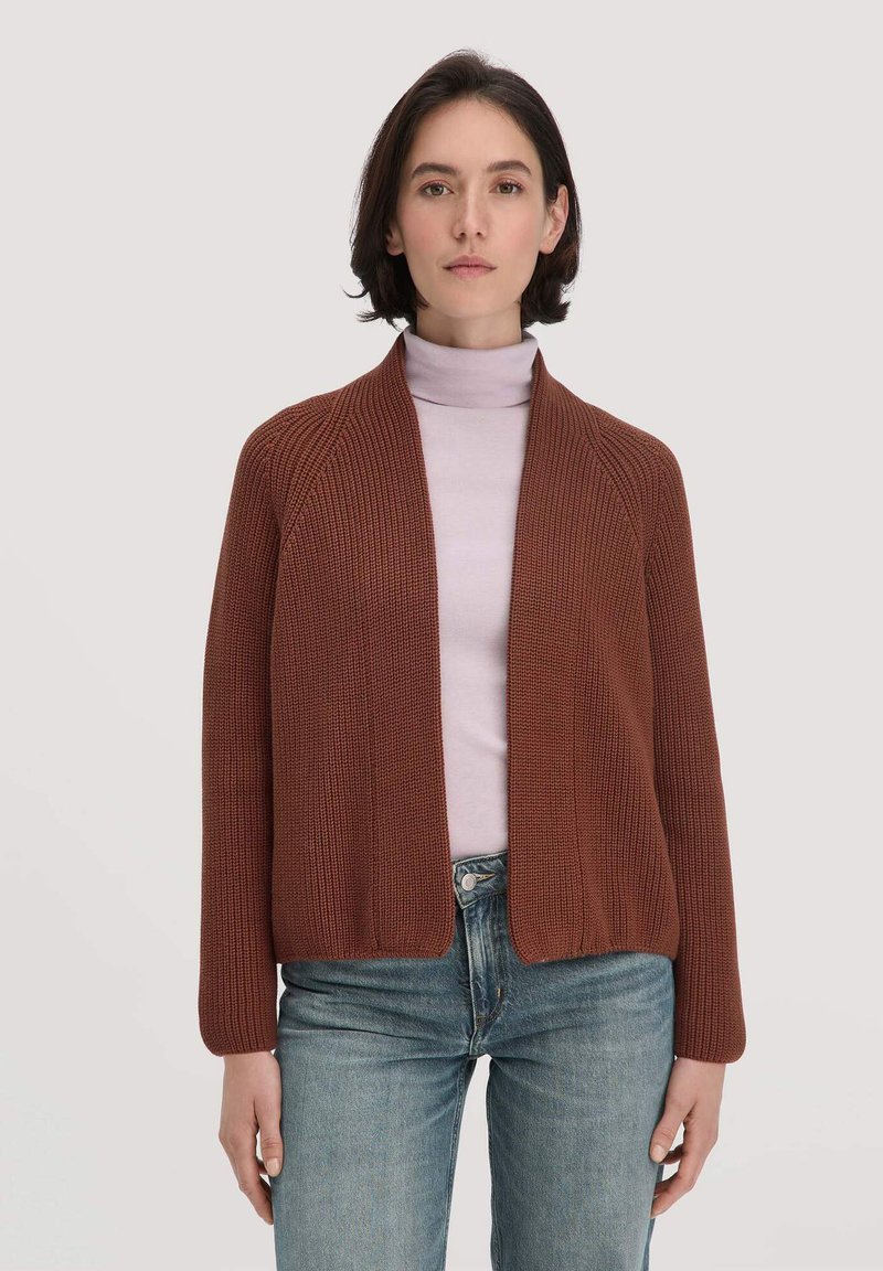 Brauner gestrickter Cardigan mit offener Front, strukturiertem Stoff und langen Ärmeln, kombiniert mit einem helllila Rollkragenpullover und blauen Jeans.