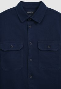 Marineblaues Button-Down-Hemd aus einem Baumwollmix, mit einem Spitzenkragen, zwei Brusttaschen und einem Knopfverschluss vorne. Glatte Textur.