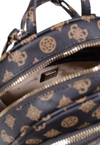 Mochila de cuero negro con patrón de logo dorado, cremalleras y interior beige. Cuenta con múltiples compartimentos y una etiqueta de marca en el interior.