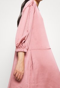 Long-sleeved dress in soft pink fabric with puffed sleeves and a relaxed fit, featuring an A-line silhouette and gathered details at the cuffs.