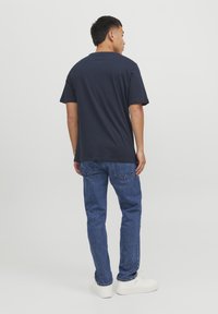 Marineblå bomulls t-skjorte med korte ermer, avslappet passform og rund hals; kombinert med blå denimjeans og hvite sneakers, sett bakfra.