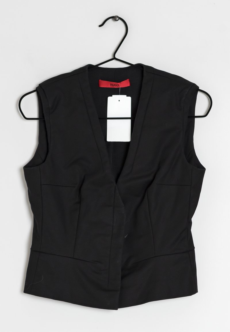 Gilet nero senza maniche con scollatura a V profonda, due tasche frontali, texture liscia e un'etichetta rossa sul collo. Etichetta attaccata con un cordino.