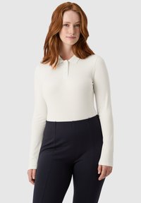 Długo-sleeve polo w kolorze off-white wykonany z prążkowanej tkaniny z zapięciem na guziki, zestawiony z wysoko taliowanymi granatowymi spodniami. Gładka tekstura, dopasowany krój.