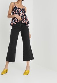 Haut peplum à motif floral en rose et noir, associé à un jean cropped noir. Le modèle porte des mules à talons blocs jaunes.