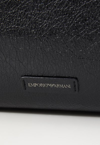 Melna ādas soma ar teksturētu virsmu. Somai ir sudraba metāla zīmola etvija ar iepresētiem vārdiem "EMPORIO ARMANI". Vienkārša taisnstūra forma.